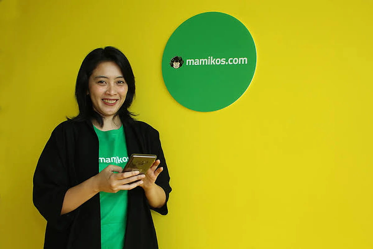 Maria Regina Anggit, pendiri Mamikos, memegang ponsel di depan logo mamikos.com