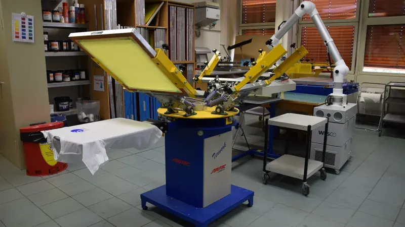 Ruang bengkel sablon kaos profesional dengan mesin sablon rotary carousel dan kaos putih di atas meja cetak