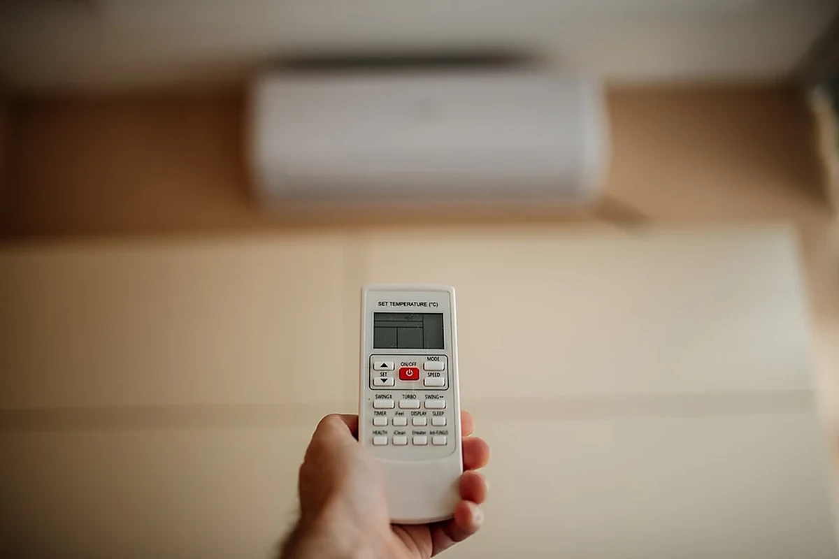 Tangan memegang remote AC mengatur suhu di dalam ruangan untuk hemat listrik